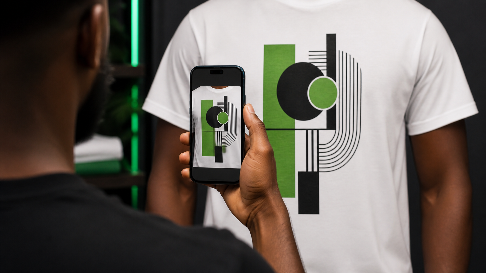 A Black customer using his phone to photograph the original graphic on a white shirt, tightly framed on the artwork